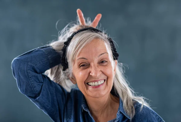 Porträt einer Seniorin, die drinnen vor dunklem Hintergrund steht und in die Kamera blickt. — Stockfoto