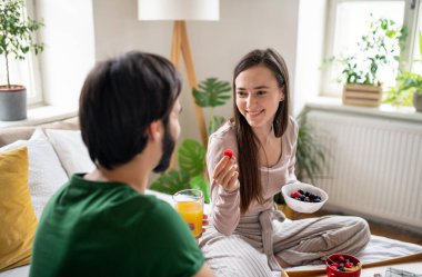 Birbirlerine aşık genç bir çift evde yatakta kahvaltı ediyor..