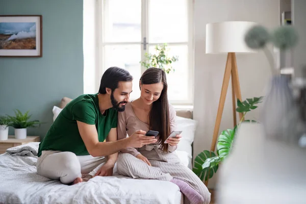 Pareja joven usando teléfonos inteligentes en la cama en el interior de casa. — Foto de Stock