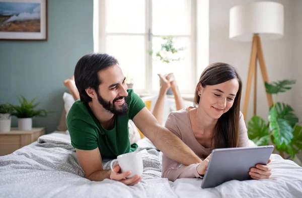 Jovem casal apaixonado usando tablet na cama dentro de casa. — Fotografia de Stock