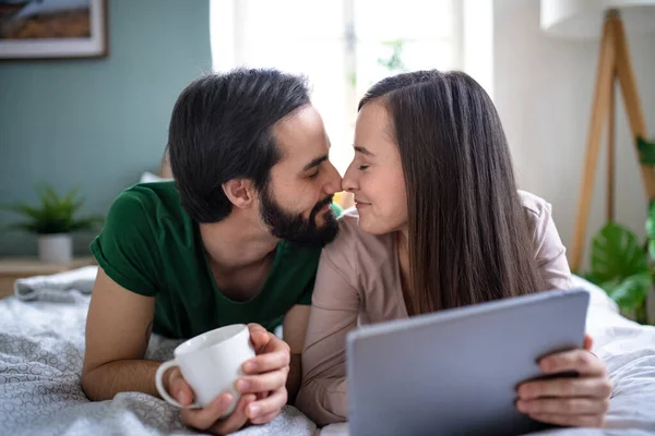Νεαρό ζευγάρι στην αγάπη χρησιμοποιώντας tablet στο κρεβάτι σε εσωτερικούς χώρους στο σπίτι. — Φωτογραφία Αρχείου
