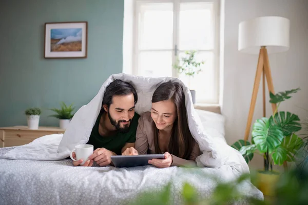 Giovane coppia innamorata utilizzando tablet sul letto al chiuso a casa. — Foto Stock