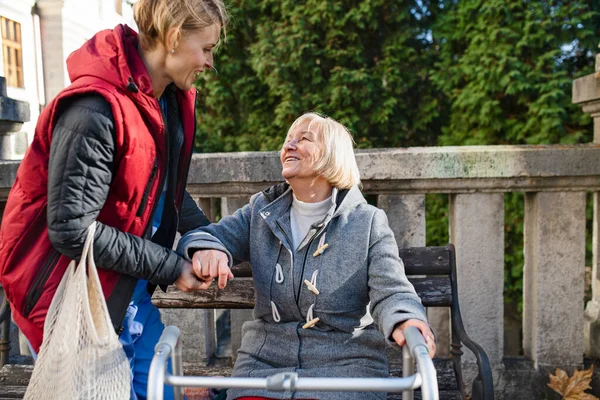 Senior kvinna med promenadram och vårdgivare utomhus sitter i parken, hjälper till att stå upp. — Stockfoto