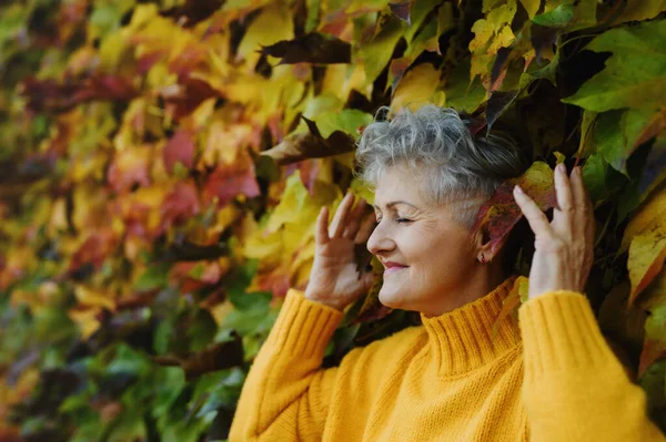 Seniorin steht draußen vor buntem, natürlichem Herbsthintergrund, die Augen geschlossen. — Stockfoto