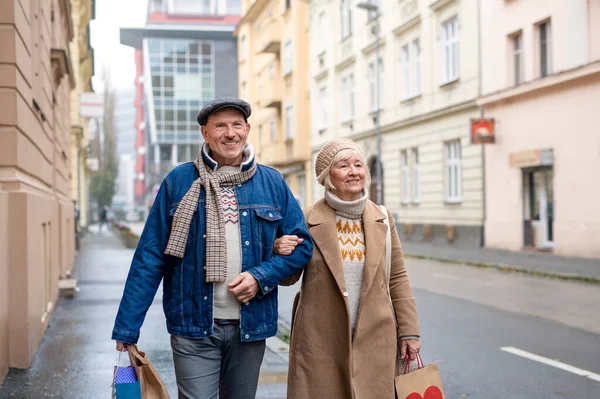 Glada äldre par promenader utomhus på gatan i staden, bär shoppingväskor. — Stockfoto