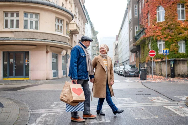 Glada äldre par promenader utomhus på gatan i staden, bär shoppingväskor. — Stockfoto