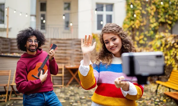 Jovem casal com smartphone fazendo vídeo para mídias sociais ao ar livre na rua. — Fotografia de Stock