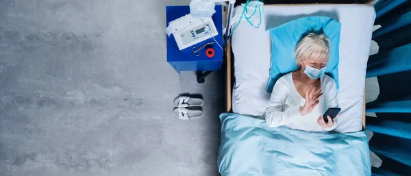 Ansicht von Frau covid-19-Patientin mit Smartphone im Krankenhausbett, Coronavirus-Konzept. — Stockfoto
