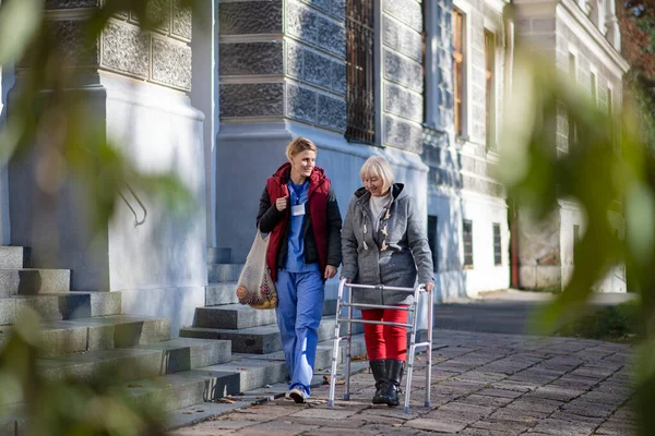 Mujer mayor con marco para caminar y cuidador al aire libre en la ciudad, compras y concepto de coronavirus. — Foto de Stock