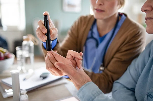 Midsectie van verzorger of zorgverlener met senior vrouwelijke patiënt, meten van de bloedglucosespiegel binnen. — Stockfoto