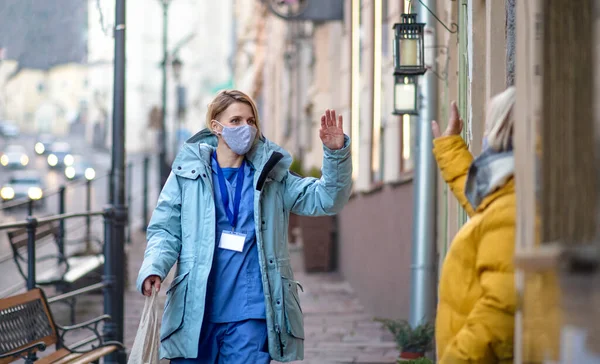 Badante all'aperto a piedi in città, salutando donna anziana. Concetto di coronavirus. — Foto Stock
