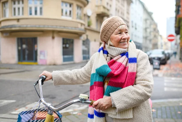 Oudere vrouw met fiets oversteek weg buiten in de stad. — Stockfoto