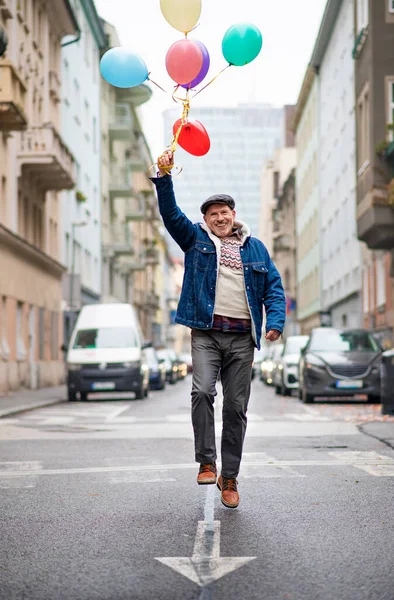 Homem sênior feliz com balões ao ar livre na rua na cidade, andando. — Fotografia de Stock