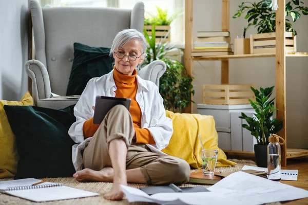 Portret van een oudere vrouwelijke architect die thuis op de vloer zit en werkt. — Stockfoto