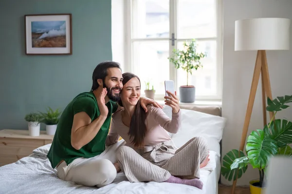 Unga par tar selfie på sängen inomhus. — Stockfoto