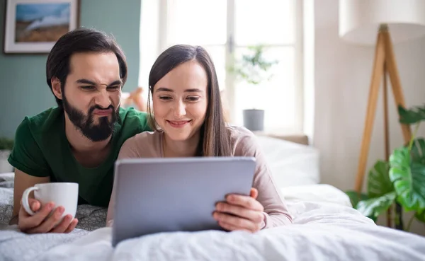 Young couple with tablet on bed indoors at home, making faces. — Stock Photo, Image