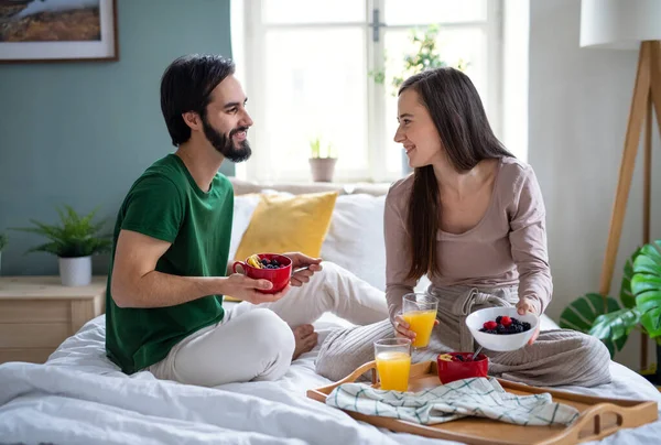 Jeune couple amoureux manger le petit déjeuner sur le lit à l'intérieur à la maison, parler. — Photo