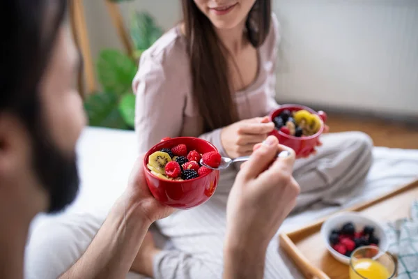 Oigenkännliga unga par kär äta frukost på sängen inomhus. — Stockfoto