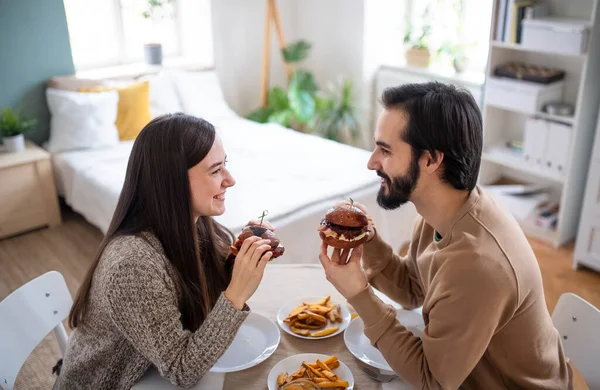 Młoda para w miłości jedząc hamburgery w domu. — Zdjęcie stockowe