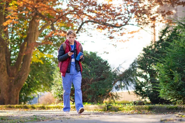 Woman caregiver, nurse or healthcare worker outdoors on the way to work, using smartphone.