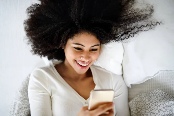 Retrato de vista superior de la mujer joven en el interior de la cama, utilizando el teléfono inteligente. — Foto de Stock