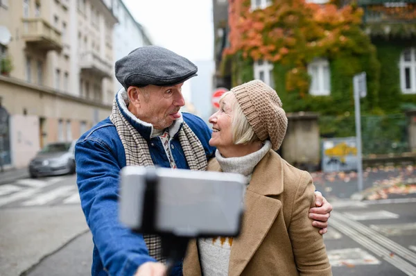 Ευτυχισμένο ζευγάρι ηλικιωμένων που περπατούν στο δρόμο στην πόλη, βγάζοντας selfie. — Φωτογραφία Αρχείου