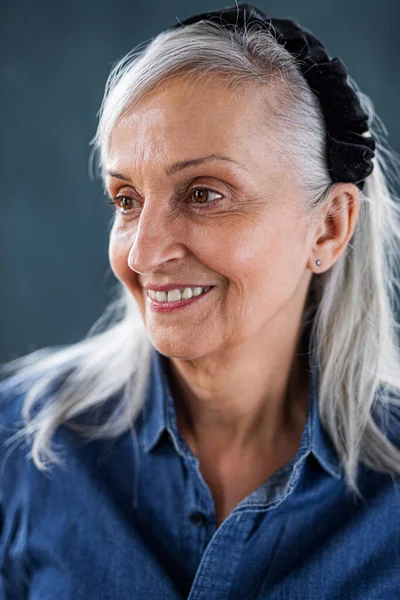 Porträt einer Seniorin, die drinnen vor dunklem Hintergrund steht. — Stockfoto