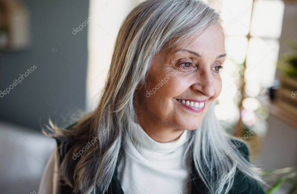 Front view portrait of happy senior woman standing indoors at home.