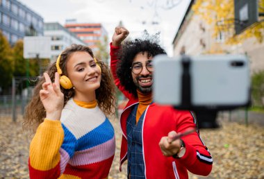 Akıllı telefonlu genç bir çift şehir parkında sosyal medya için video çekiyor..