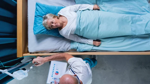 Draufsicht auf Arzt und Patientin mit iv-Tropfen im Bett im Krankenhaus. — Stockfoto