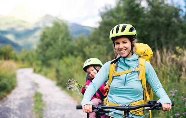 Mother with small daughter cycling outdoors in summer nature, looking at camera. — Stock Photo, Image