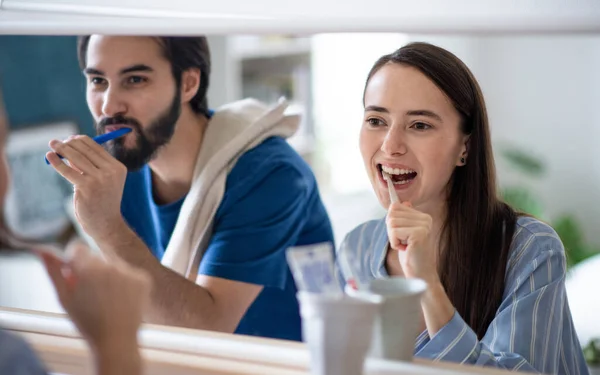 Unga par borsta tänderna framför spegeln inomhus. — Stockfoto