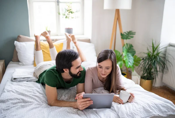 Ungt par i kærlighed ved hjælp af tablet på sengen indendørs derhjemme. - Stock-foto