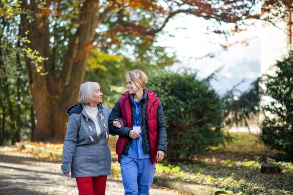 Senior woman and caregiver outdoors on a walk in park, talking. — Stock Photo, Image
