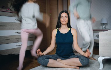 Anne evde yoga meditasyon egzersizi yapıyor, kızlar oynuyor..