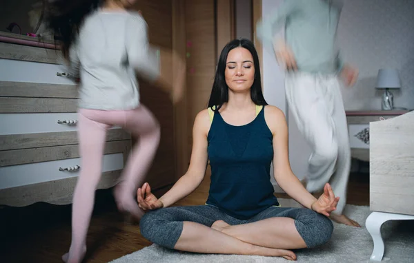 Mamma gör yoga meditation motion inomhus hemma, döttrar leker. — Stockfoto