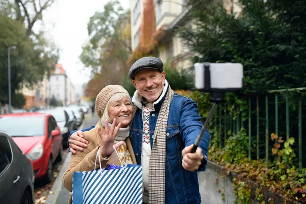 Šťastný starší pár procházky venku na ulici ve městě, přičemž selfie. — Stock fotografie