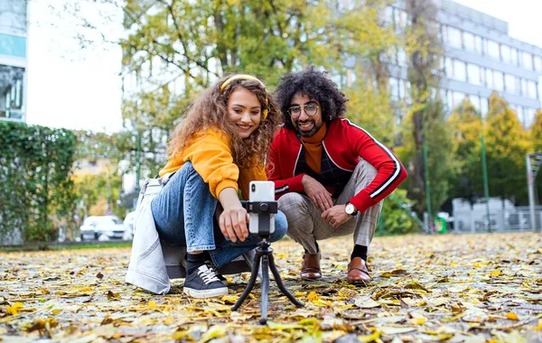 公園で屋外ソーシャルメディアのためのビデオを作るスマートフォンを持つ若いカップル. — ストック写真