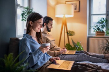 Yatakta dizüstü bilgisayar kullanan genç çift, ev ofis konsepti..