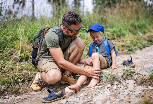 Father with small son on trek outdoors in summer nature, falling and scratched knee concept. — Stock Photo, Image