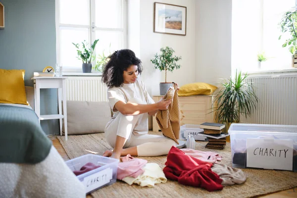 Jonge vrouw sorteren garderobe binnen thuis, liefdadigheid donatie concept. — Stockfoto