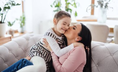 Anne ve küçük kızı evdeki kanepede oturup öpüşüyorlar..