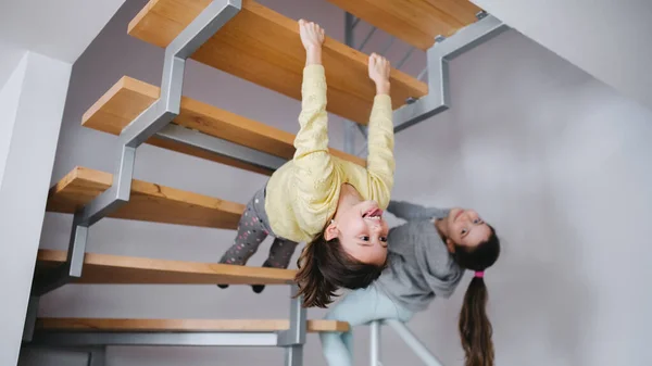 Duas meninas pequenas irmãs dentro de casa, se divertindo sob escada. — Fotografia de Stock