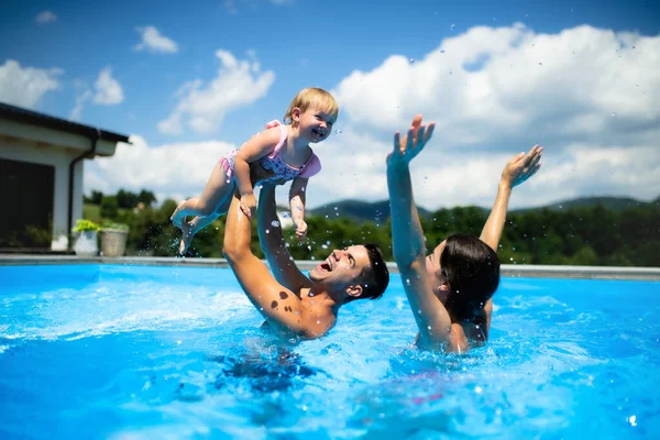 Молодая семья с маленькой дочкой в бассейне на открытом воздухе в саду, играя. — стоковое фото
