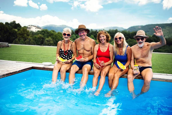 Skupina veselých seniorů sedících venku u bazénu na dvorku a dívajících se do kamery. — Stock fotografie