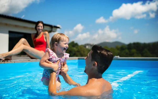 Young family with small daughter in swimming pool outdoors in backyard garden, playing. — 图库照片