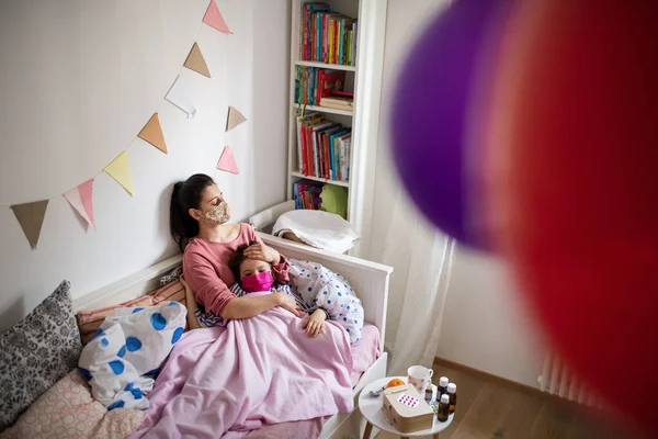 Zmęczona matka opiekuje się chorą małą córką w łóżku w domu, koncepcja koronawirusa. — Zdjęcie stockowe