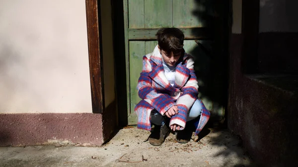 Pobre menina pequena triste com casaco grande ao ar livre na frente da casa, conceito de pobreza. — Fotografia de Stock