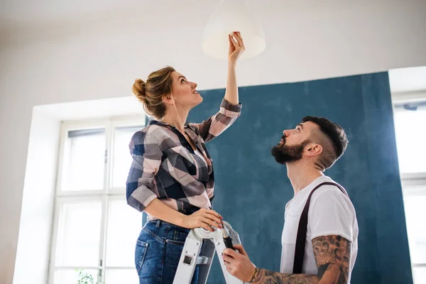 Mid adults couple changing light bulb indoors at home, relocation and diy concept. — Stock Photo, Image