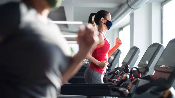 Yüz maskeli kadın spor salonunda koşu bandında egzersiz yapıyor, koronavirüs konsepti.. — Stok fotoğraf